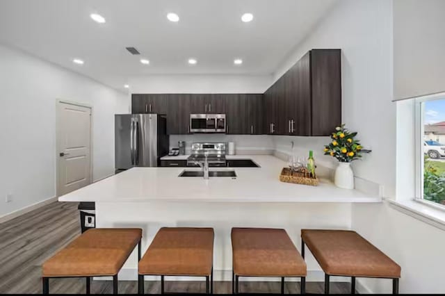 kitchen with dark brown cabinetry, stainless steel appliances, a kitchen bar, and light countertops