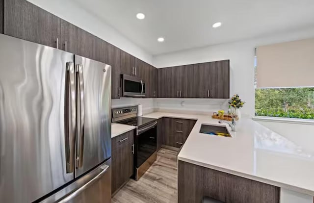 kitchen featuring light countertops, appliances with stainless steel finishes, a sink, and dark brown cabinets