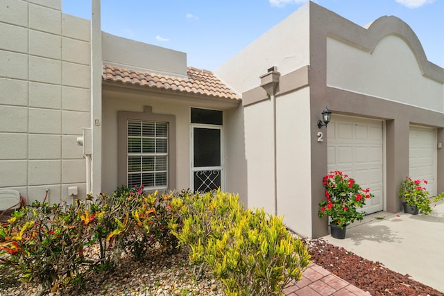 view of side of property with driveway, an attached garage, a tile roof, and stucco siding