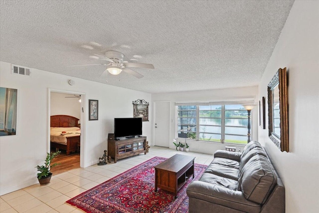 living room with light tile patterned floors, a ceiling fan, visible vents, and a textured ceiling