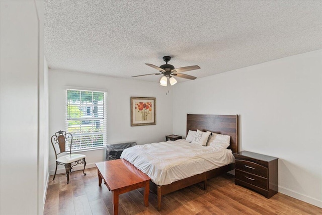 bedroom featuring a ceiling fan, a textured ceiling, baseboards, and wood finished floors