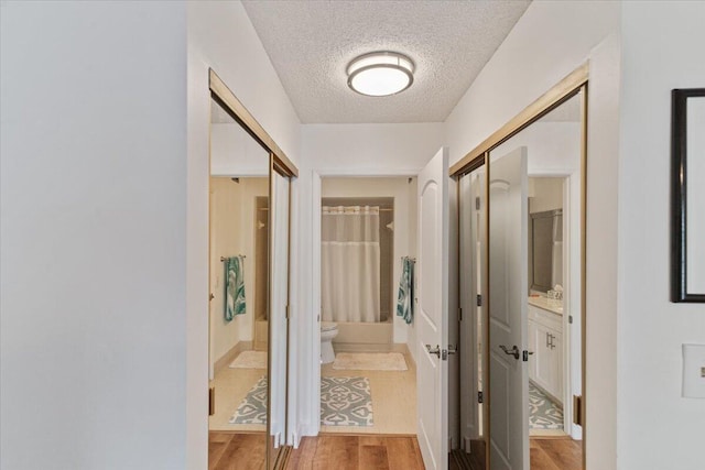 corridor featuring a textured ceiling and light wood finished floors