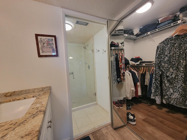 full bathroom with a walk in closet, a stall shower, a textured ceiling, vanity, and wood finished floors