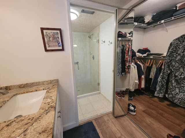 full bathroom with a textured ceiling, wood finished floors, vanity, a shower stall, and a walk in closet