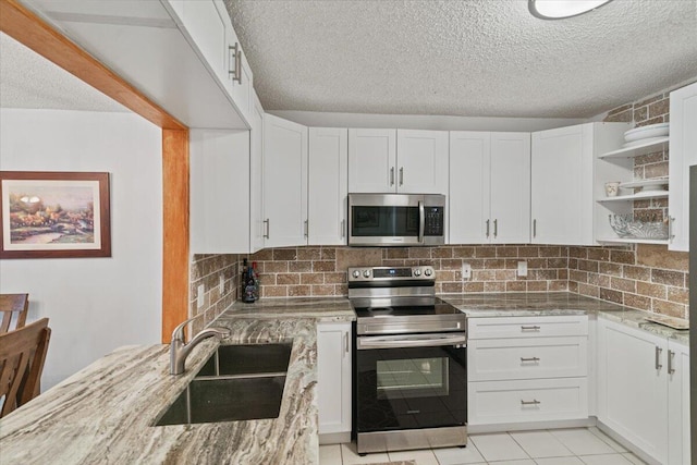 kitchen featuring light stone counters, stainless steel appliances, a sink, white cabinets, and decorative backsplash