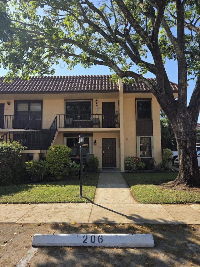 townhome / multi-family property featuring a front yard, a tile roof, a balcony, and stucco siding