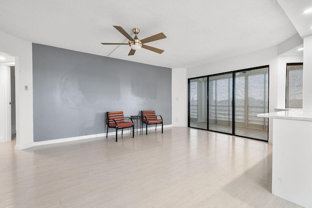 living area with light wood-type flooring, a textured ceiling, baseboards, and a ceiling fan