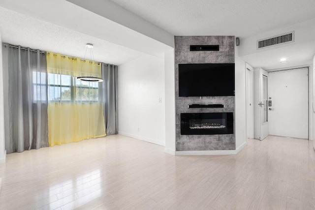 unfurnished living room with visible vents, a fireplace, a textured ceiling, and wood finished floors