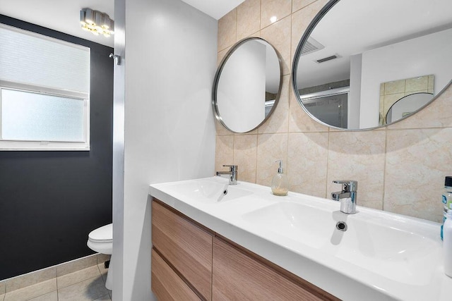 bathroom with tile walls, double vanity, visible vents, toilet, and a sink