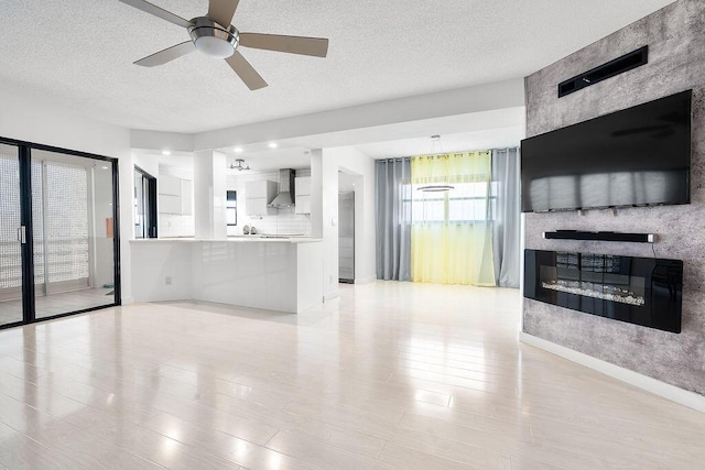 living area with a textured ceiling, a fireplace, a ceiling fan, and baseboards