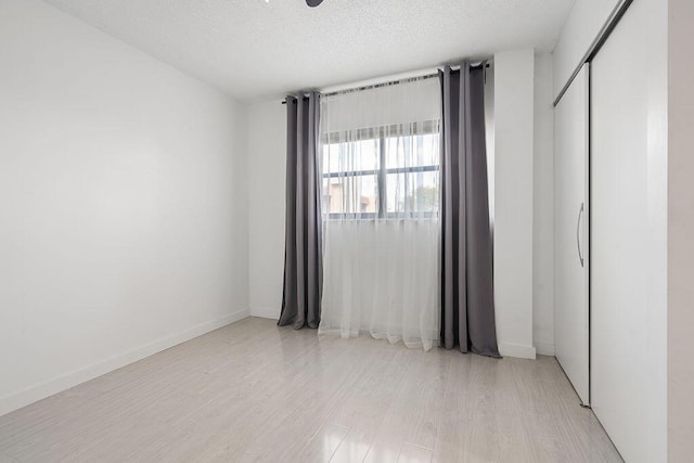 spare room featuring light wood-style flooring, baseboards, and a textured ceiling