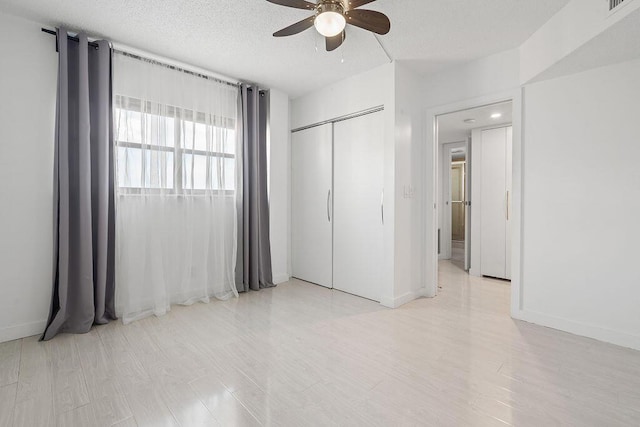 unfurnished bedroom with light wood-type flooring, a closet, a textured ceiling, and baseboards