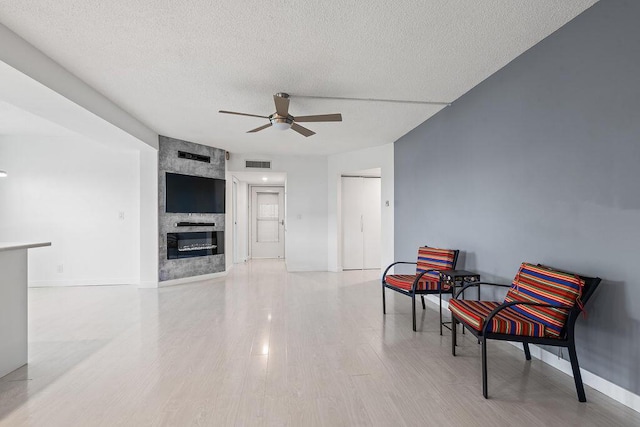 sitting room with a fireplace, visible vents, light wood-style floors, a ceiling fan, and a textured ceiling