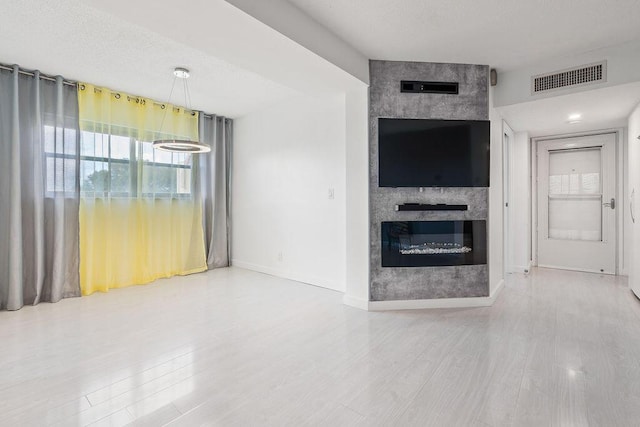 unfurnished living room featuring visible vents, a fireplace, baseboards, and wood finished floors