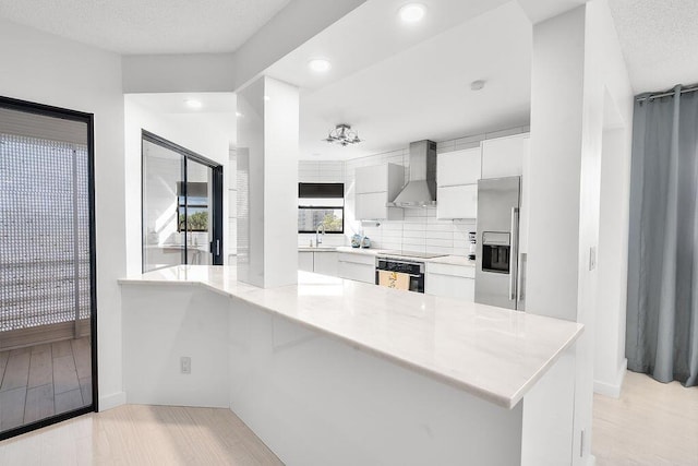 kitchen featuring stainless steel appliances, white cabinets, wall chimney range hood, modern cabinets, and a peninsula