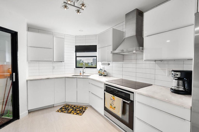 kitchen featuring white cabinets, wall chimney exhaust hood, oven, black electric cooktop, and light countertops