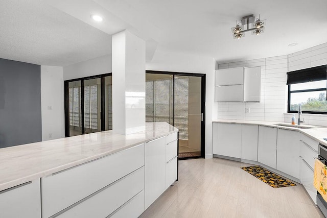 kitchen with a sink, white cabinets, decorative backsplash, light wood finished floors, and modern cabinets