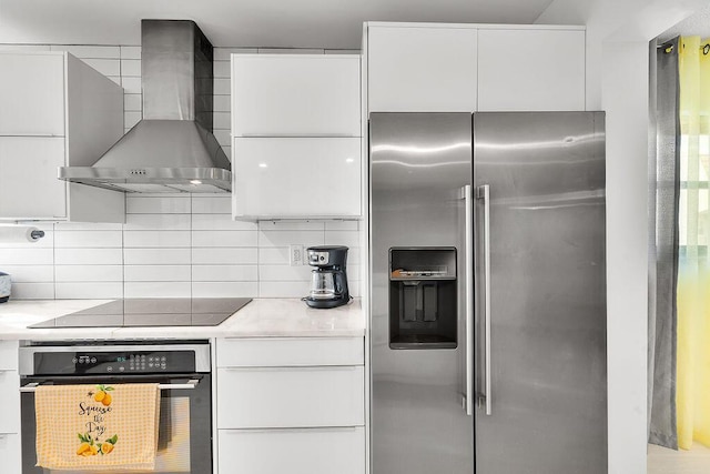 kitchen with white cabinets, light countertops, appliances with stainless steel finishes, wall chimney exhaust hood, and tasteful backsplash