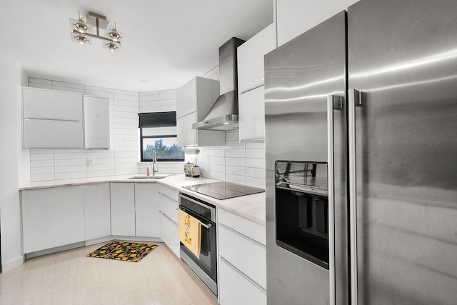 kitchen featuring wall chimney exhaust hood, appliances with stainless steel finishes, light countertops, white cabinetry, and a sink