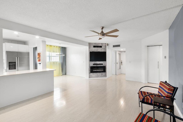 living area featuring a large fireplace, visible vents, ceiling fan, a textured ceiling, and light wood-style floors