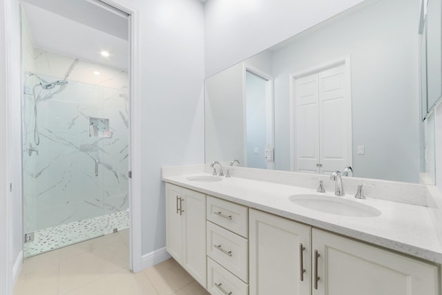 bathroom featuring a marble finish shower, double vanity, a sink, tile patterned flooring, and baseboards