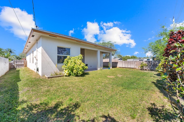 rear view of property with a fenced backyard, a lawn, and stucco siding