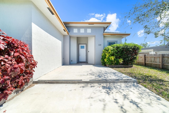 entrance to property featuring fence, a patio, and stucco siding