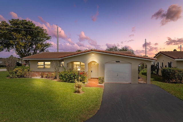 mediterranean / spanish house with driveway, a tile roof, an attached garage, a front lawn, and stucco siding