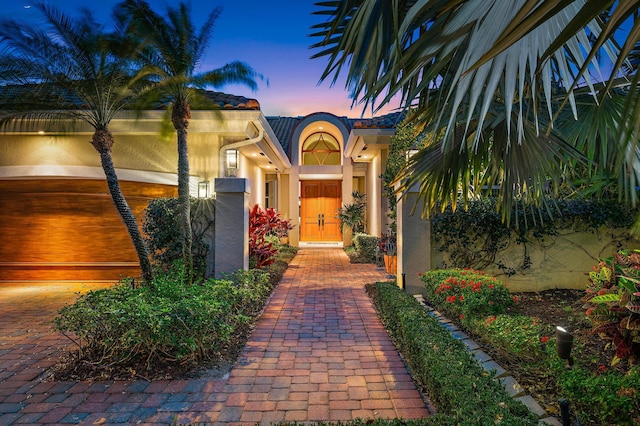 exterior entry at dusk featuring a tiled roof and stucco siding