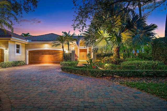 view of front of house featuring a garage, a tile roof, decorative driveway, and stucco siding