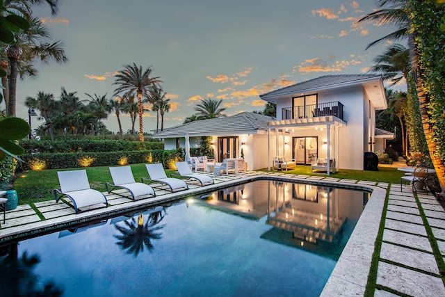 back of house featuring french doors, an outdoor pool, a patio area, a balcony, and a yard