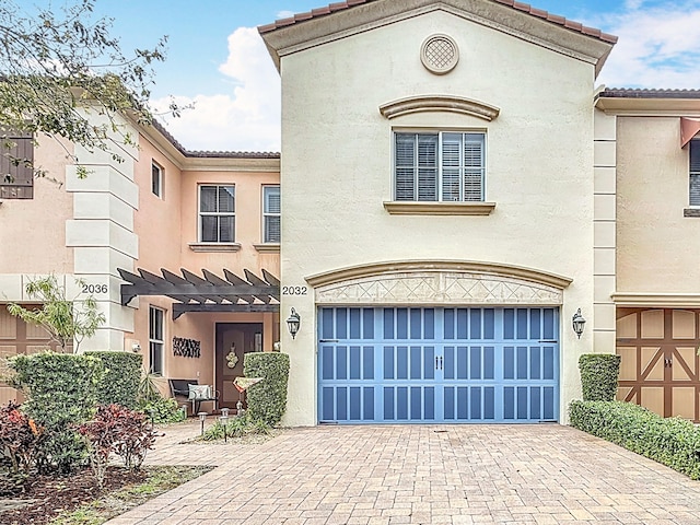 view of front of property with an attached garage, a tile roof, decorative driveway, and stucco siding