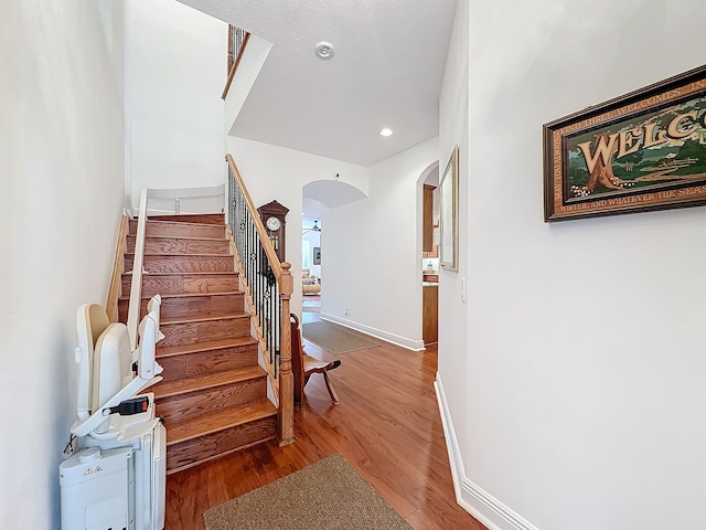 stairs with baseboards, arched walkways, wood finished floors, and recessed lighting