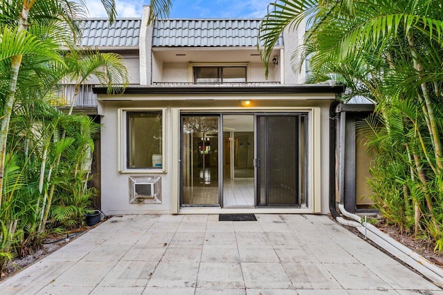 entrance to property featuring a patio area, a tiled roof, a wall mounted air conditioner, and stucco siding