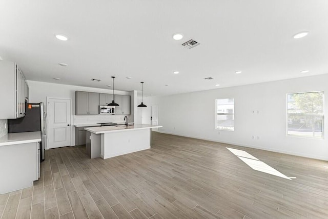 kitchen with a kitchen island with sink, visible vents, light countertops, appliances with stainless steel finishes, and gray cabinets