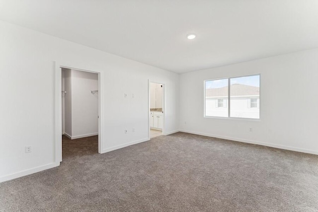 unfurnished bedroom featuring ensuite bathroom, carpet flooring, baseboards, a spacious closet, and a closet