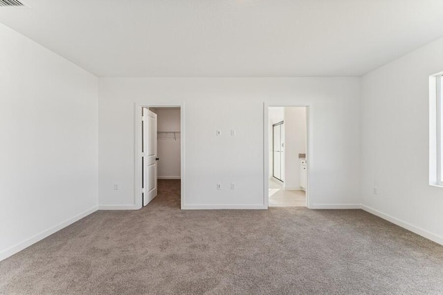 unfurnished bedroom with a closet, carpet flooring, a walk in closet, and baseboards