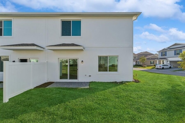 rear view of house featuring a yard, fence, and stucco siding