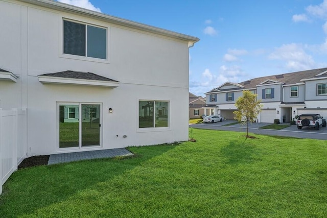 rear view of property with a residential view, a lawn, driveway, and stucco siding