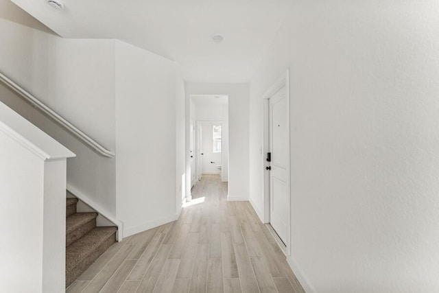 corridor with light wood-type flooring, stairs, and baseboards