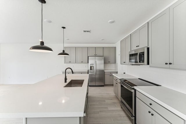 kitchen with stainless steel appliances, a sink, visible vents, gray cabinets, and decorative backsplash