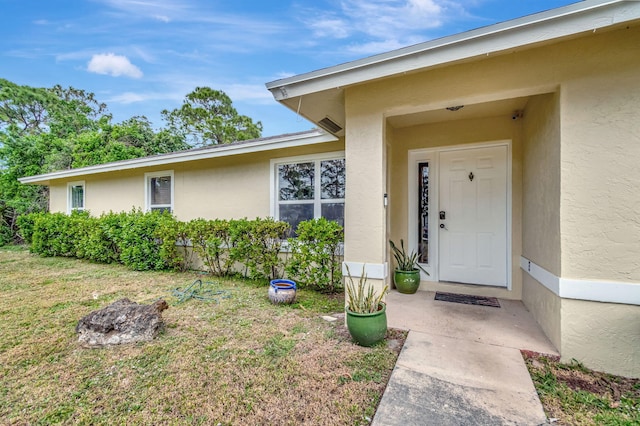 doorway to property with a lawn and stucco siding