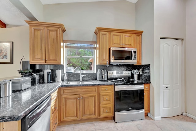 kitchen featuring light tile patterned floors, appliances with stainless steel finishes, dark stone countertops, a sink, and backsplash