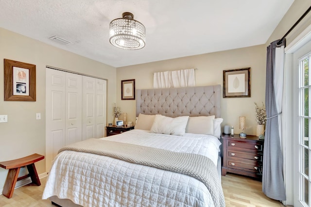 bedroom with a closet, visible vents, a textured ceiling, light wood-type flooring, and a notable chandelier