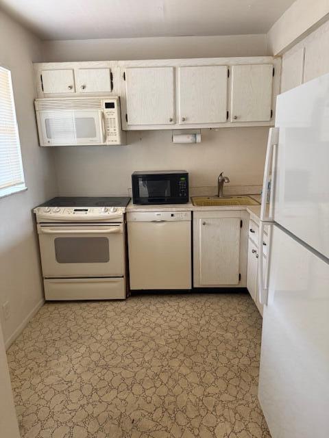 kitchen with white appliances, white cabinets, light countertops, light floors, and a sink