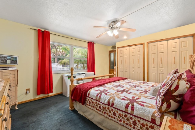 bedroom with two closets, dark carpet, ceiling fan, a textured ceiling, and baseboards