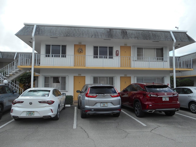 view of front of house featuring uncovered parking, stucco siding, stairs, and mansard roof