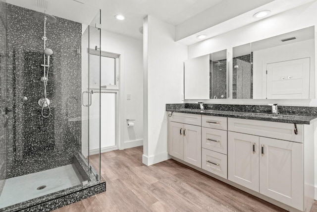 bathroom with double vanity, a sink, a shower stall, wood finished floors, and baseboards