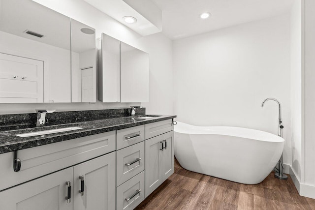 bathroom featuring a soaking tub, visible vents, a sink, and wood finished floors