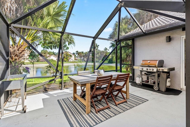 view of patio featuring glass enclosure, outdoor dining area, grilling area, and a water view